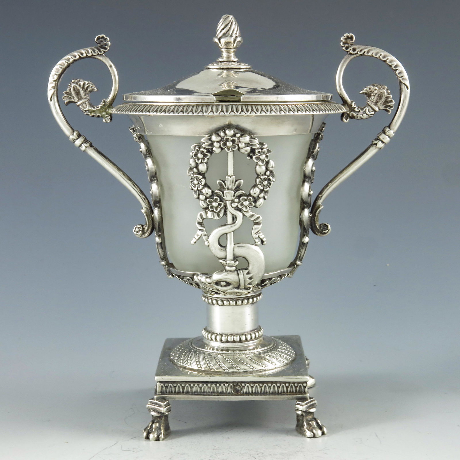 M ?, Paris circa 1830, a French silver mustard pot, in: M ?, Paris circa 1830, a French silver mustard pot, in the Empire style, the frosted glass container within a cage of alternating cast wreath and dolphin and reticulated daisy scroll pilasters, flaked