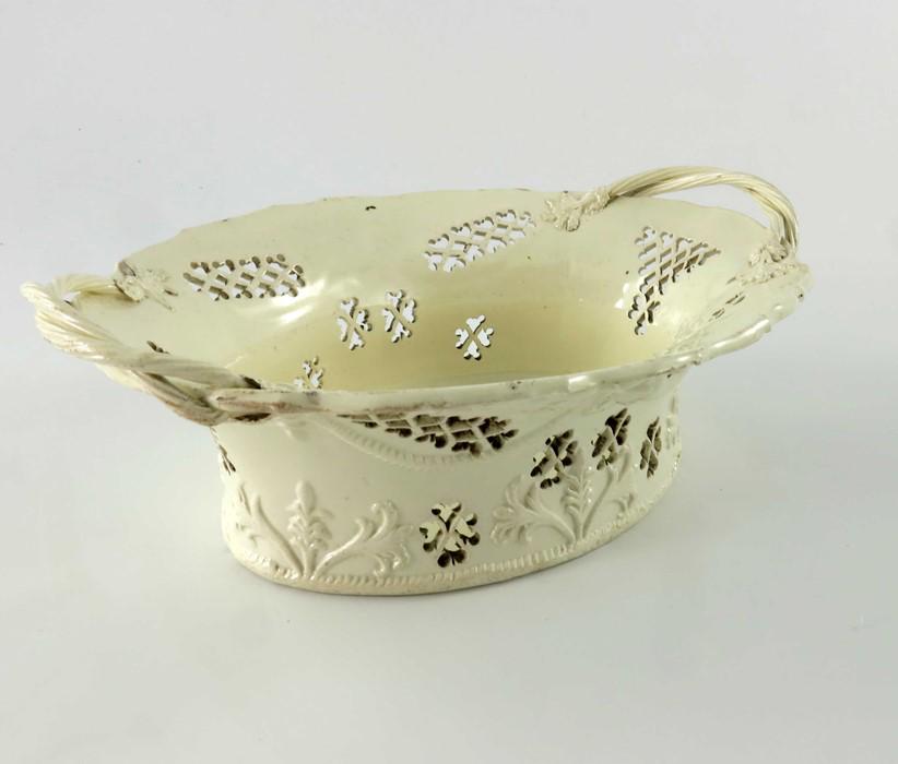 A creamware reticulated basket, circa 1785, ogee rimmed: A creamware reticulated basket, circa 1785, ogee rimmed oval flared form, pierced trellis sections, relief moulded with winged heads and laurel swags, rope twist handles and feathered borders, 25cm lo