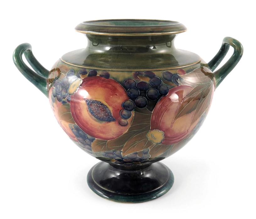 William Moorcroft for James MacIntyre, a twin handled: William Moorcroft for James MacIntyre, a twin handled Pomegranate on ochre vase, circa 1910, footed squat amphora form, flambe tinted rim, underglaze green signature, 23cm high