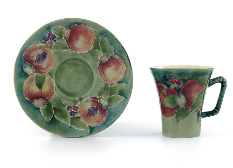 William Moorcroft for James MacIntyre, a Pomegranate: William Moorcroft for James MacIntyre, a Pomegranate coffee cup and saucer, circa 1911, trumpet form with angled cane moulded handle, celadon ground, underglaze green signature and monogram (2)