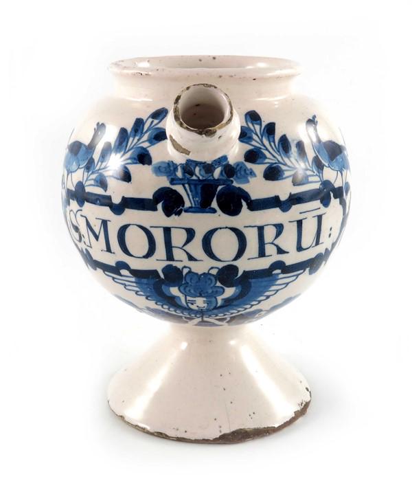 A Lambeth Delft wet drug jar, globular form on a: A Lambeth Delft wet drug jar, globular form on a spreading foot, loop handle and squat spout, circa 1720, decorated in blue with a scrolling strapwork label inscribed S.MORORU: (syrup of mulberry), su