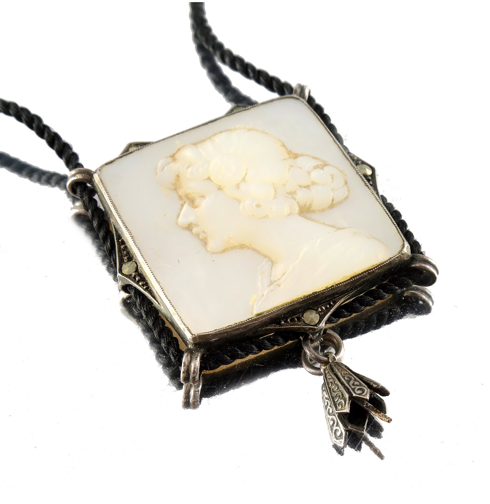 An Art Nouveau silver, mother-of-pearl and marcasite: An Art Nouveau silver, mother-of-pearl and marcasite necklace, the square plaque with the bust of a maiden in profile, within a silver mount, on a knotted silk cord, length of pendant 5cm, length of c