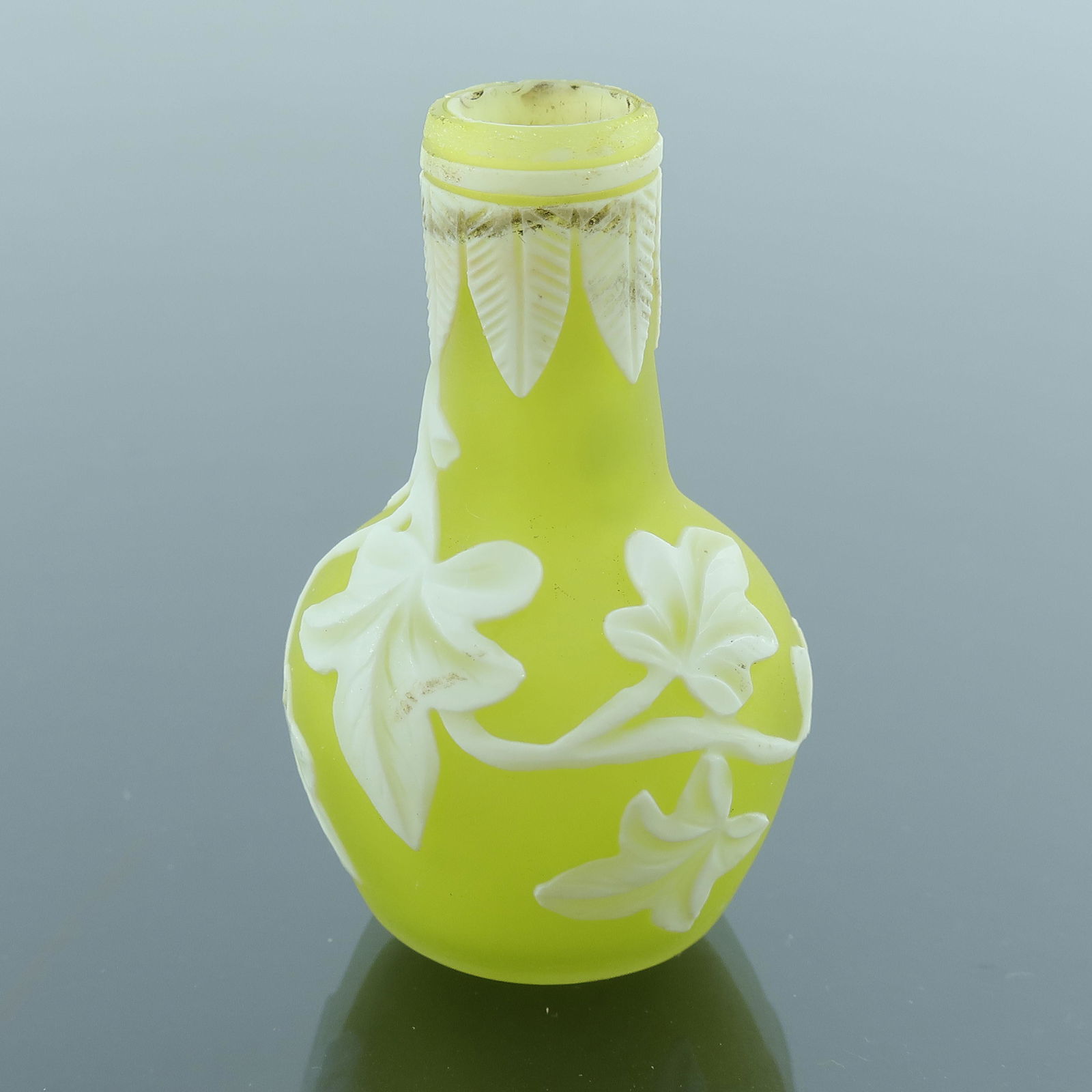 Thomas Webb, a miniature cameo glass vas: Thomas Webb, a miniature cameo glass vase, circa 1880, bottle form, white over cased yellow on white, carved with ivy leaves below a lappet border, 5cm high
