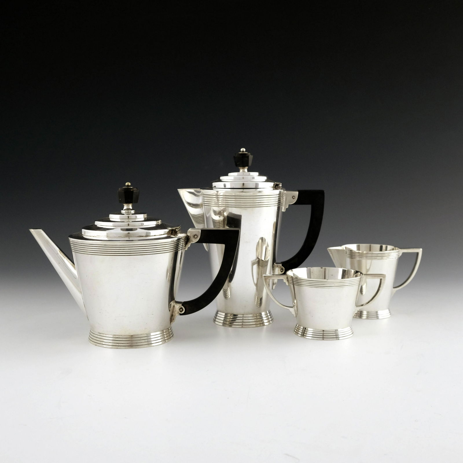 Keith Murray for Mappin and Webb, an Art: Keith Murray for Mappin and Webb, an Art Deco four piece tea set, circa 1932, conical stepped form with concentric ring decoration, ebonised handled and finials, stamped marks W27681, 20cm high (4)