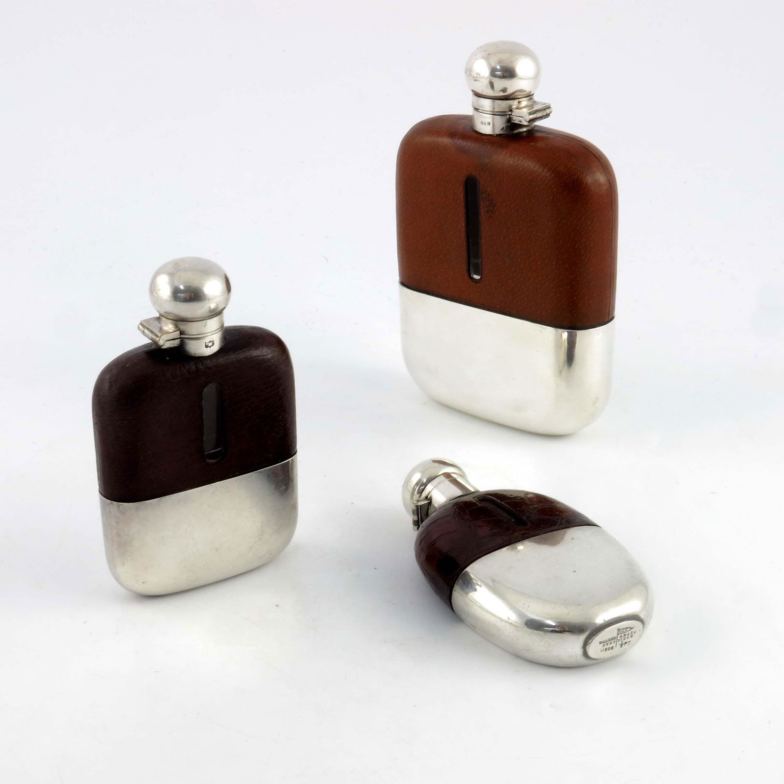 Three George V silver plated and leather: Three George V silver plated and leather hip flasks, Walker and Hall and James Dixon and Sons, various sizes, one with alligator leather, each with bayonet hinged caps, 17.5cm high (3)