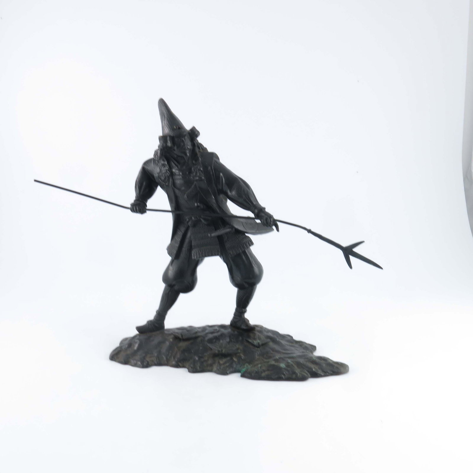 A Japanese bronze study of a Samurai, Me: A Japanese bronze study of a Samurai, Meiji period, 1868-1912, modelled standing in battle pose in full headdress and robes with a spear, on a raised naturalistic plinth, height 34cm, width 31cm