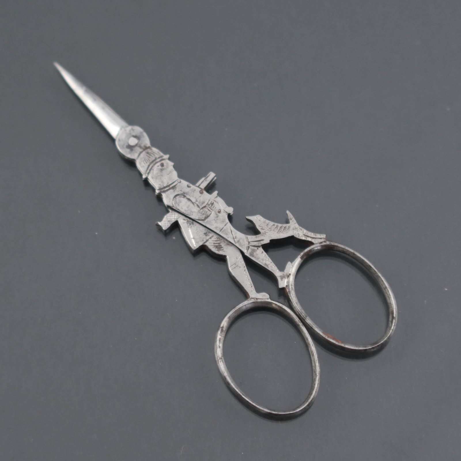 Antique Scissors: the huntsman and his d: Antique Scissors: the huntsman and his dog, a pair of novelty steel scissors, the shank forming a male figure with his shotgun under his arm and his hunting dog pawing at his knee, marked on both inne