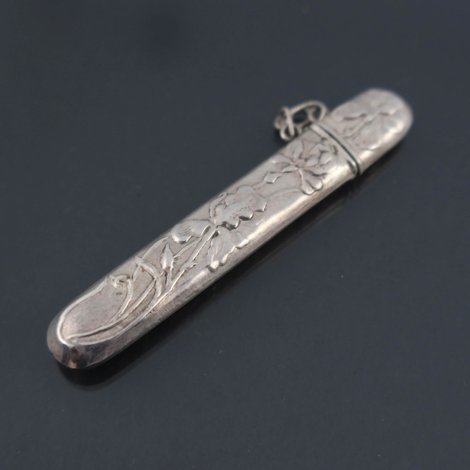 Four embossed white metal needle cases,: Four embossed white metal needle cases, one of Art Nouveau design with iris and a dragonfly, indistinctly marked inside, with side chain to secure the lid to the body; the second quite round with etch