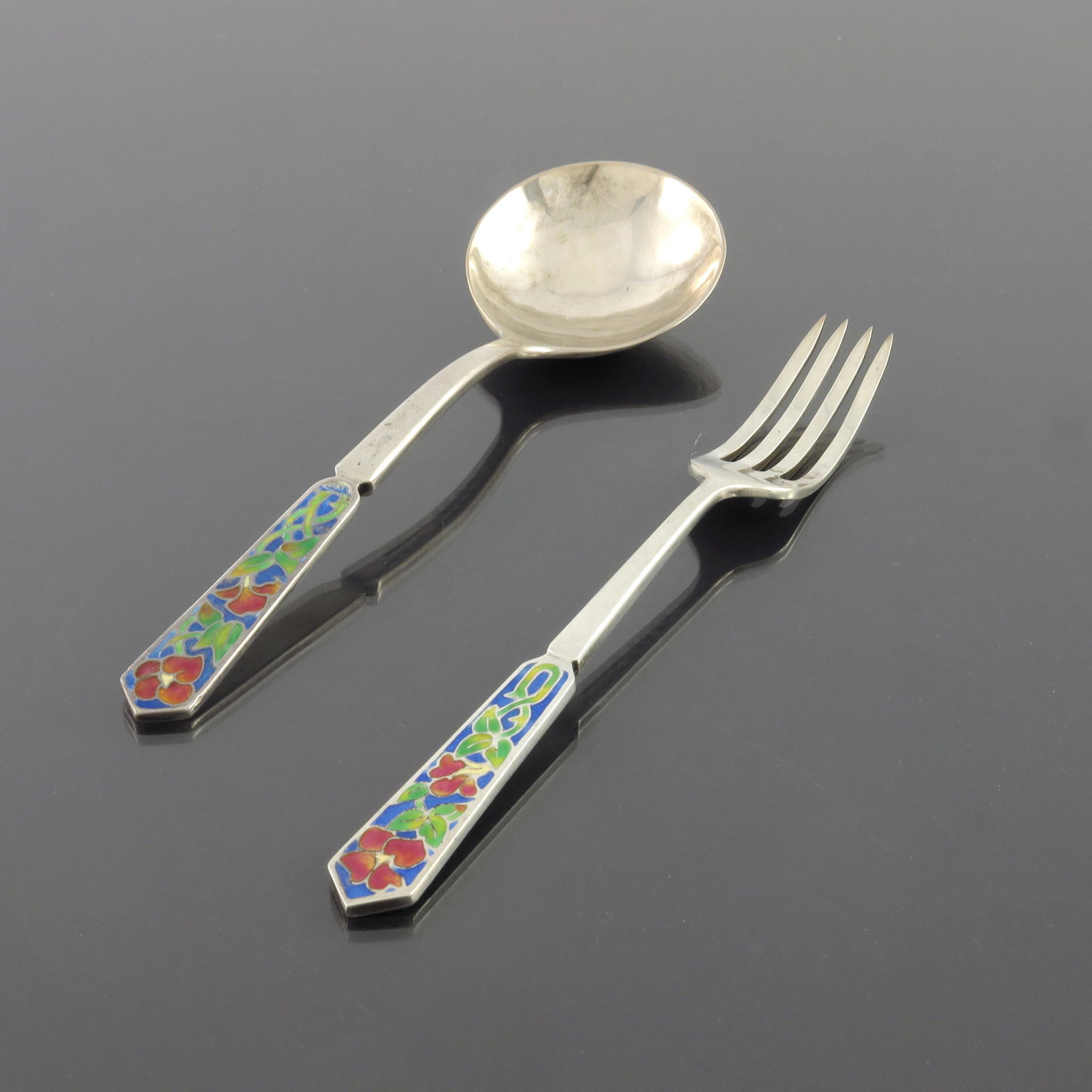 Bernard Instone, an Arts and Crafts silv: Bernard Instone, an Arts and Crafts silver and enamelled spoon and fork, Birmingham 1929/1930, the champleve enamel terminals decorated with stylised knotted flowers, in green, red and blue, planished