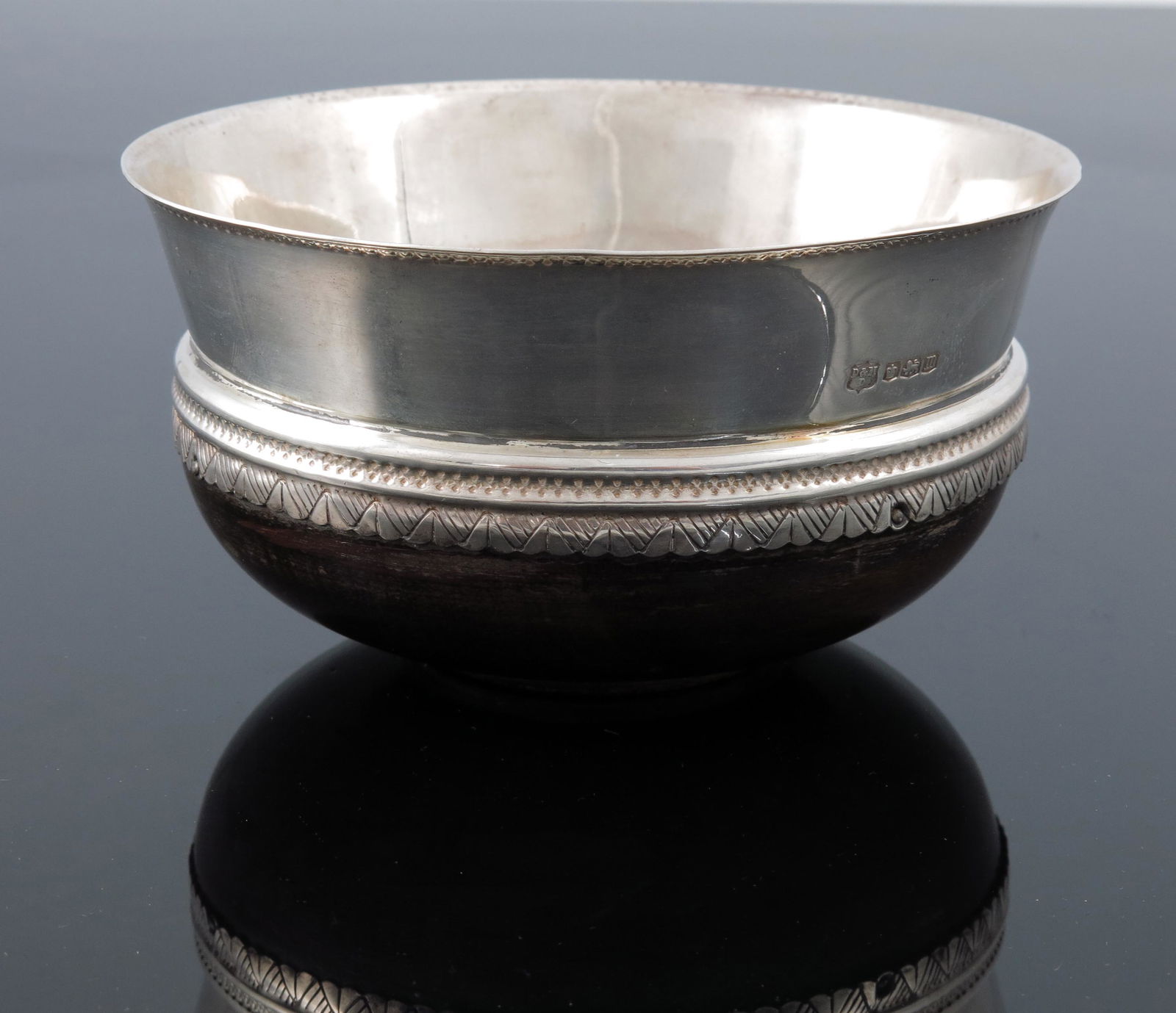 A George V silver mazer bowl, D and M Da: A George V silver mazer bowl, D and M Davis, Sheffield 1929, turned wooden base with flared rim, geometric bands and punched beading, 12cm diameter