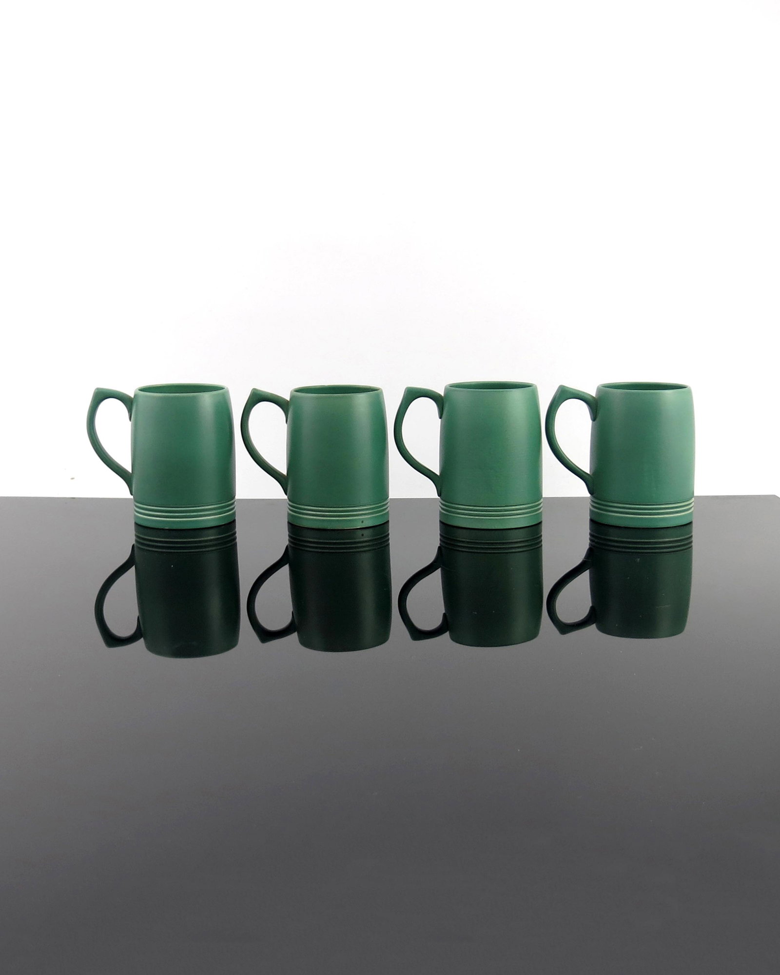 Keith Murray for Wedgwood, four matt gre: Keith Murray for Wedgwood, four matt green glazed beer mugs, circa 1934, incised concentric ring decoration to the base, printed facsimile signatures, 12cm high (4)