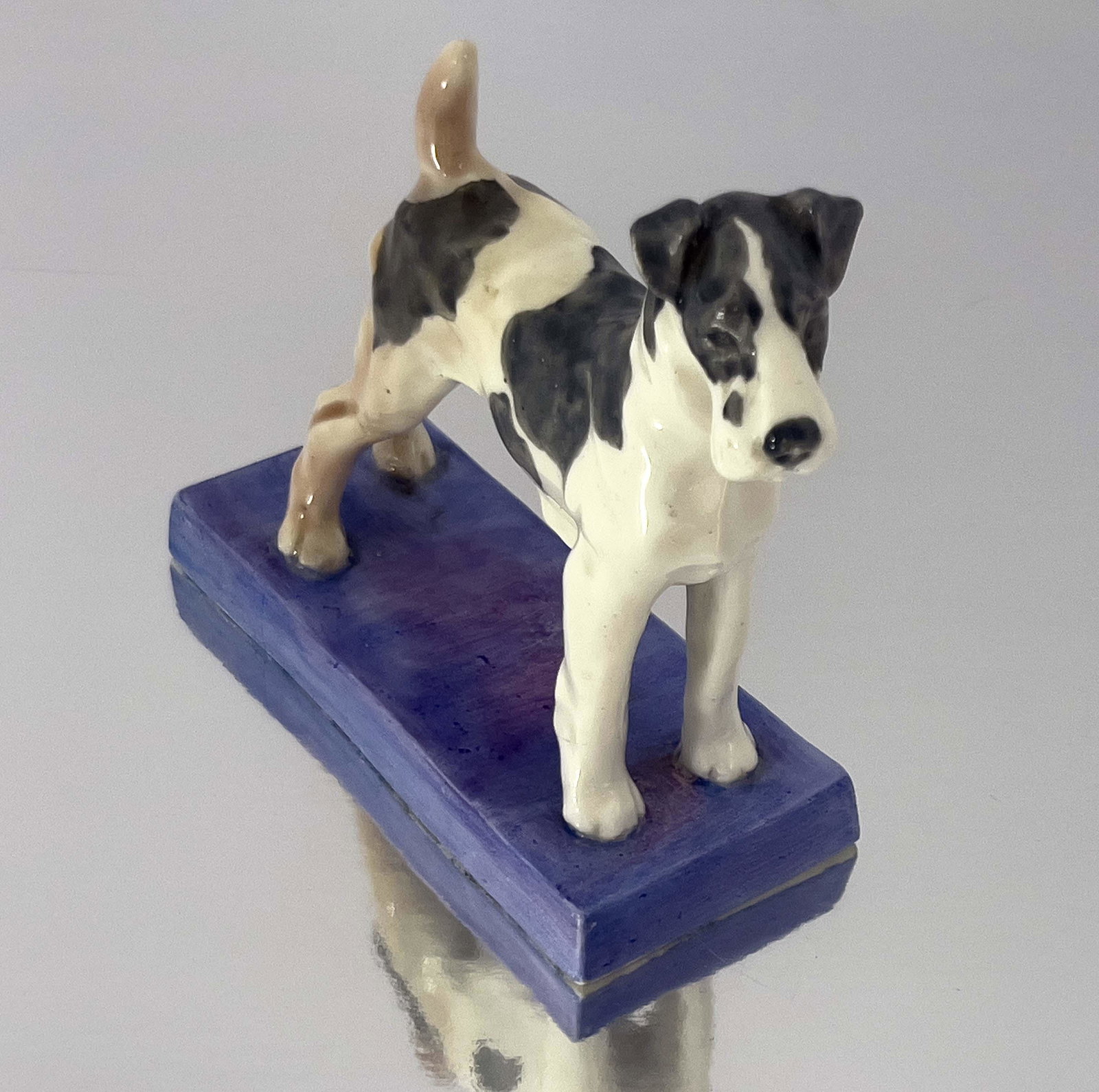 Doris Lindner for Royal Worcester, a fig: Doris Lindner for Royal Worcester, a figure of a Terrier, model 2870, on blue purple base, together with a figure group of three spaniel puppies, model 3130, 9.5cm high (2)
