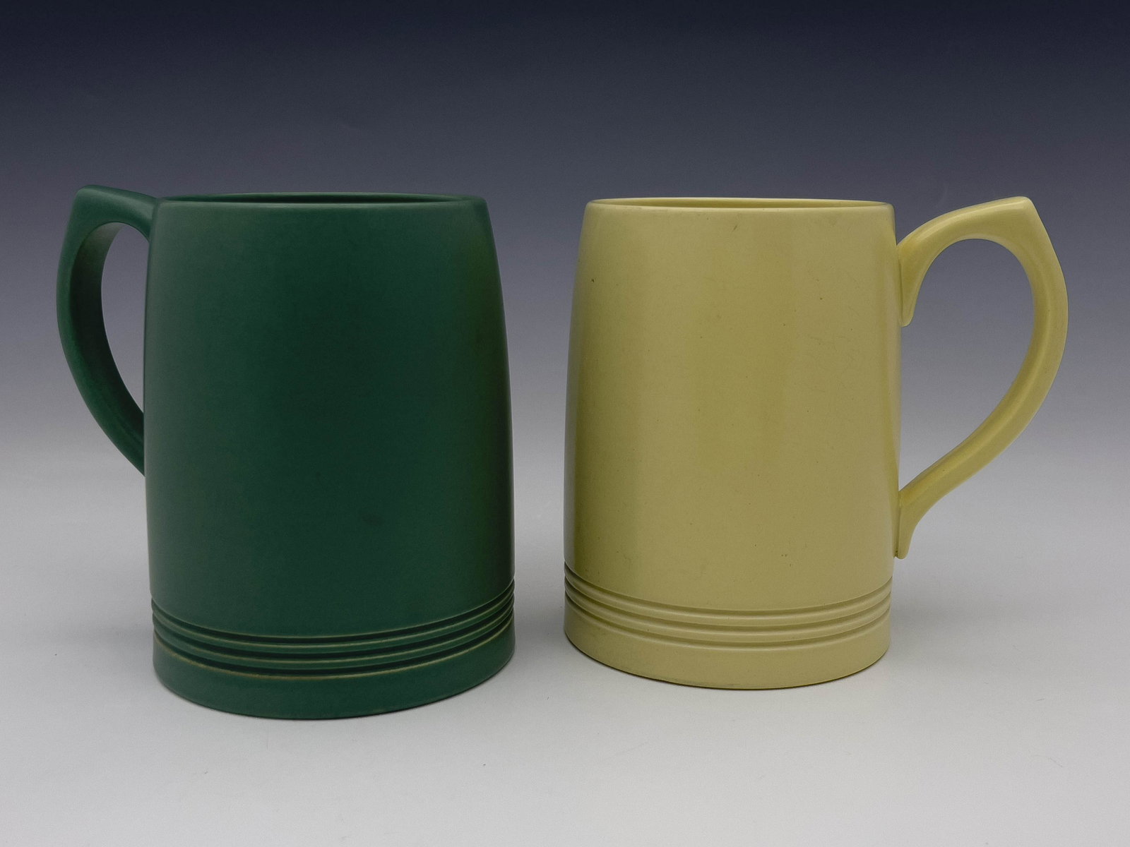 Keith Murray for Wedgwood, two Art Deco: Keith Murray for Wedgwood, two Art Deco beer mugs or tankards, circa 1934, one in matt green, the other in semi-gloss straw, each with incised concentric ring decoration, printed and facsimile signatu