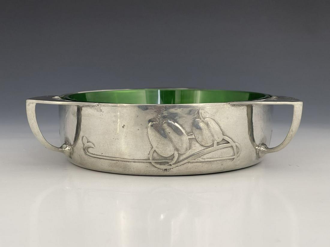 Archibald Knox for Liberty and Co., an A: Archibald Knox for Liberty and Co., an Arts and Crafts Tudric pewter and glass butter dish, model 0162, circular form, cast in relief with knotted budding tendrils, three open bracket handles and gree