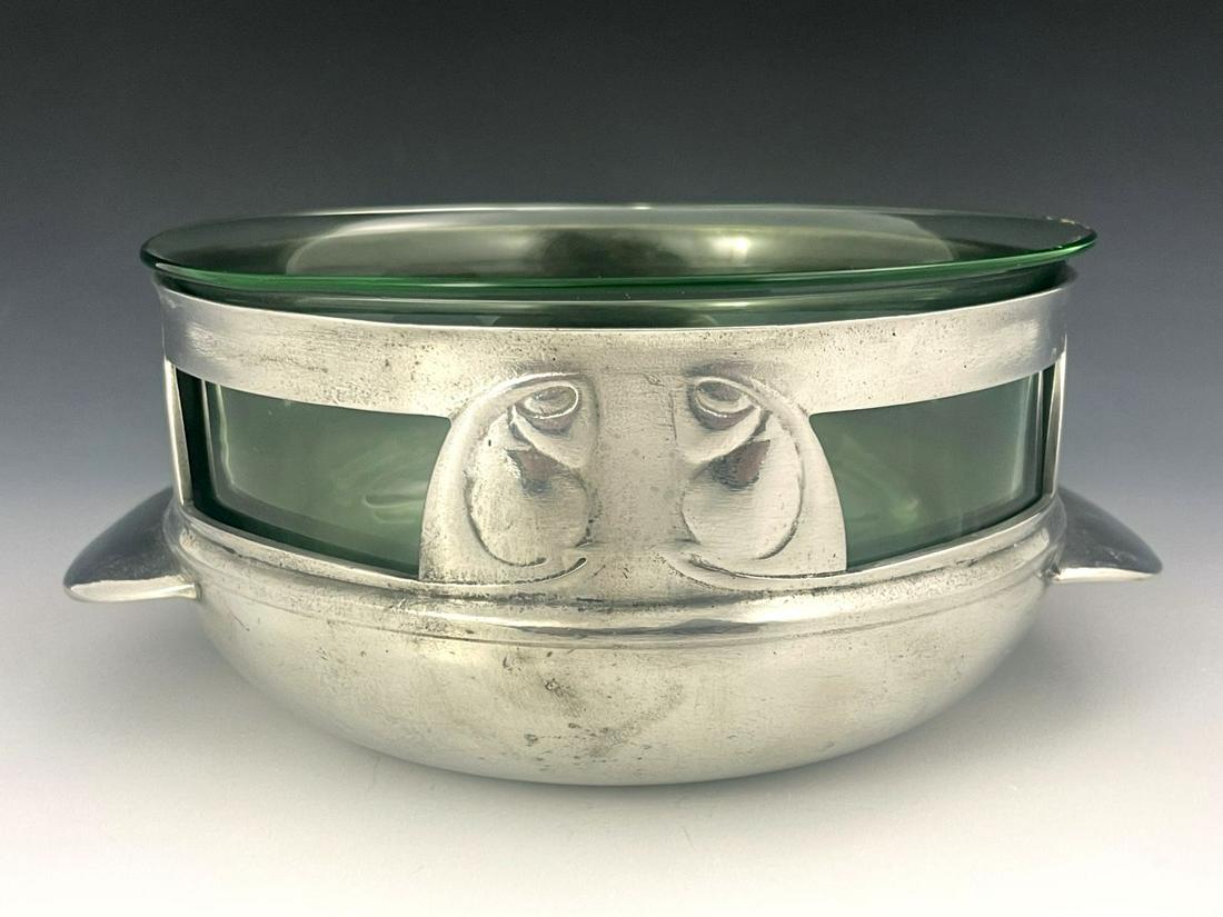 Archibald Knox for Liberty and Co., an A: Archibald Knox for Liberty and Co., an Arts and Crafts Tudric pewter and glass bowl, model 0320, twin handled squat bulbous form, four open panels between cast foiled bud motifs, tongue handles, green