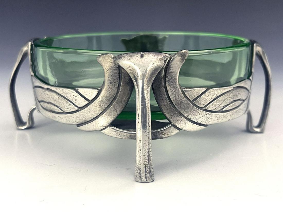 Archibald Knox for Liberty and Co., an A: Archibald Knox for Liberty and Co., an Arts and Crafts Tudric pewter and glass butter dish, model 0575, circular form, four open tendril bracket legs between incised basket weave swags, green glass li