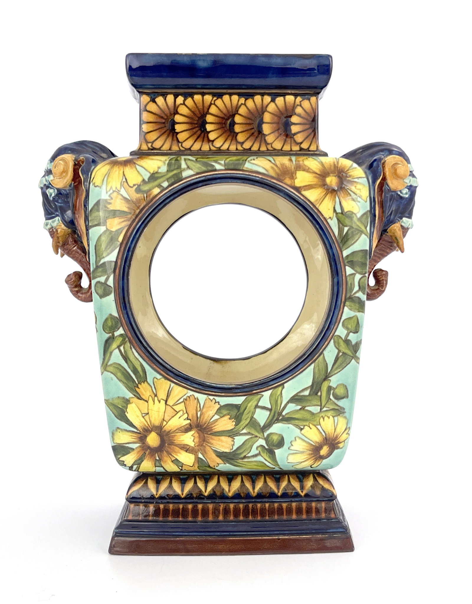 Mary Butterton for Doulton Lambeth, a fa: Mary Butterton for Doulton Lambeth, a faience clock case, plinth form with relief moulded elephant mask handles, painted with flowers, between geometric foliate borders, painted marks, 26cm high