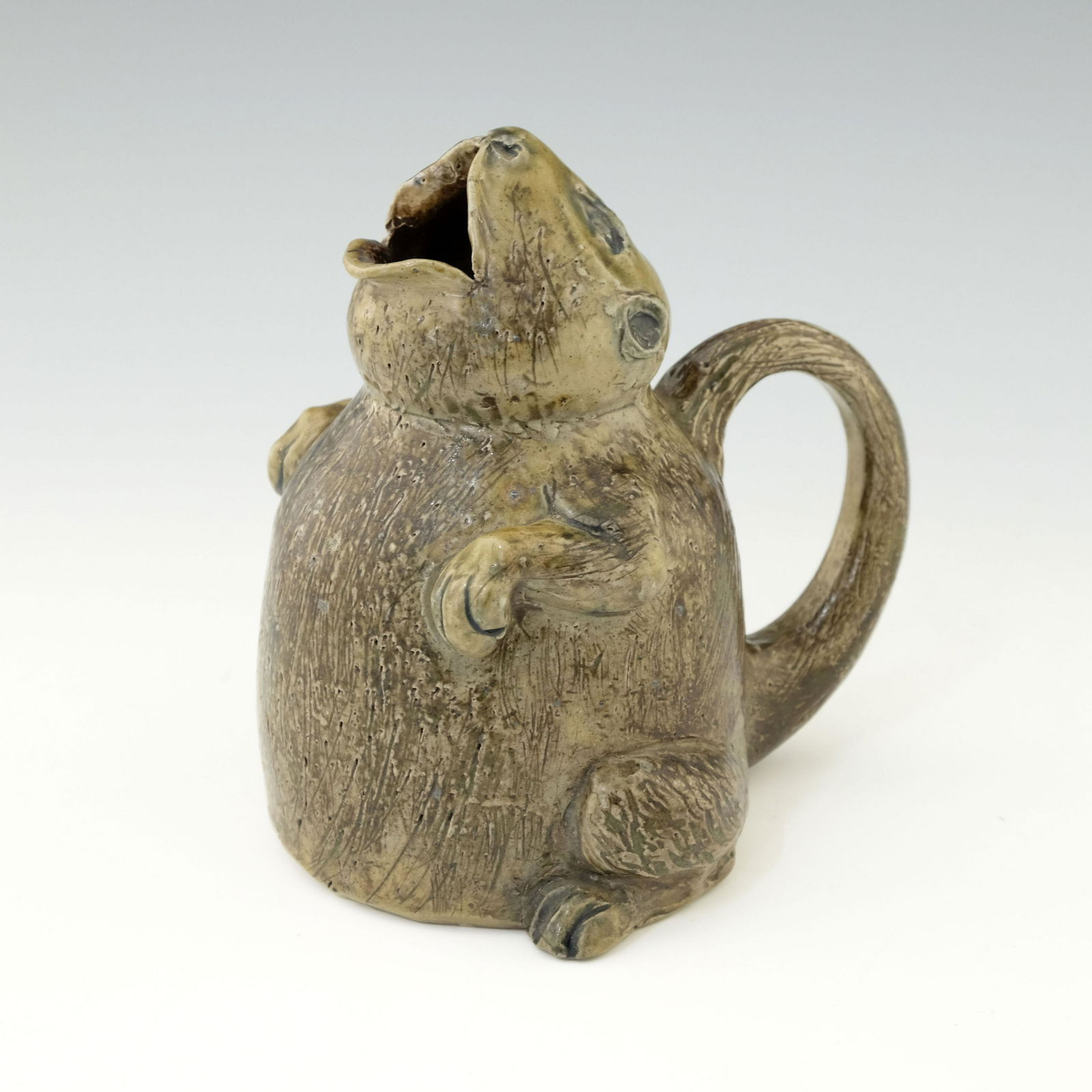 Robert Wallace Martin for Martin Brother: Robert Wallace Martin for Martin Brothers, a grotesque novelty stoneware spoon warmer, circa 1880, modelled as a characterful rodent, squatting with head raised and mouth open, the tail forming the ha