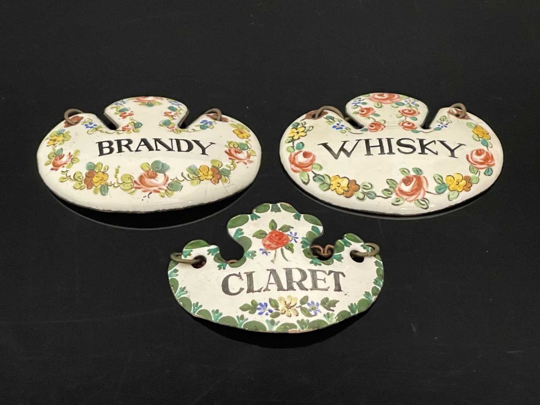 A group of three nineteenth-century Cont: A group of three nineteenth-century Continental enamelled escutcheon form wine labels or bottle tickets, decorated in polychrome enamel with floral garlands and titled, 'BRANDY', WHISKY, and 'CLARET',