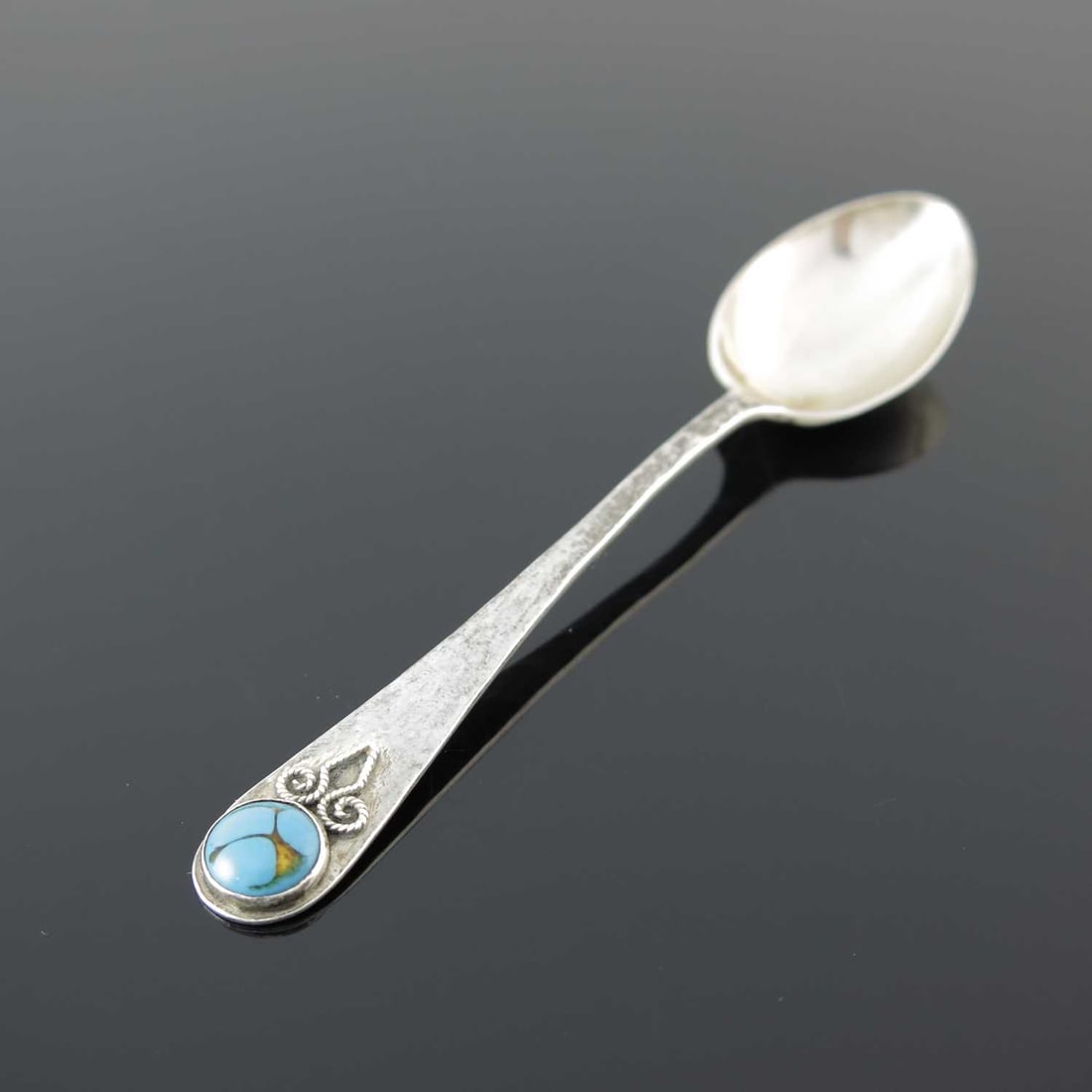 Bernard Instone. A George V Arts & Craft: Bernard Instone. A George V Arts & Crafts silver teaspoon, with planished stem and matt bowl, the terminal with applied filigree scrolls, inset with a polished turquoise cabochon, Bernard Instone, Bir