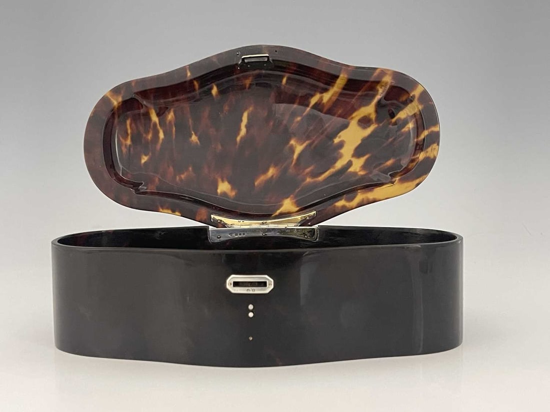 A George V tortoiseshell and silver-moun: A George V tortoiseshell and silver-mounted jewellery box, of shaped rectangular form, the lobed body with silver escutcheon and hinge, Charles & Richard Comyns, London 1919, length 23cm approx