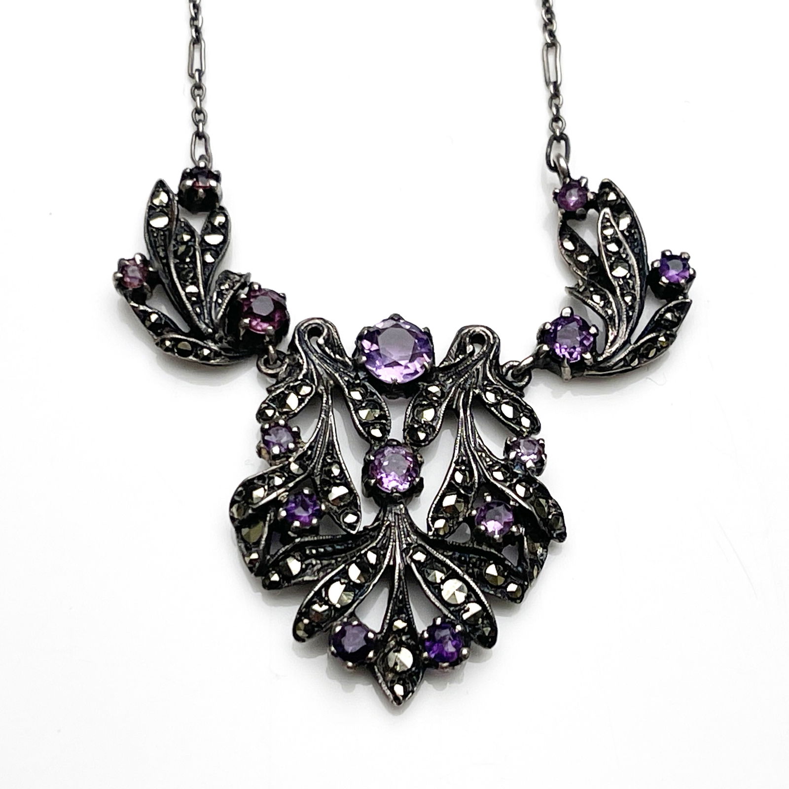 Bernard Instone, an Art Deco silver, marcasite and amethyst necklace, the ope foliate pendant with: Bernard Instone, an Art Deco silver, marcasite and amethyst necklace, the ope foliate pendant with graduated leaves and rose cut stones, suspended on two further links and a chain, 3.5cm long, 13.7g