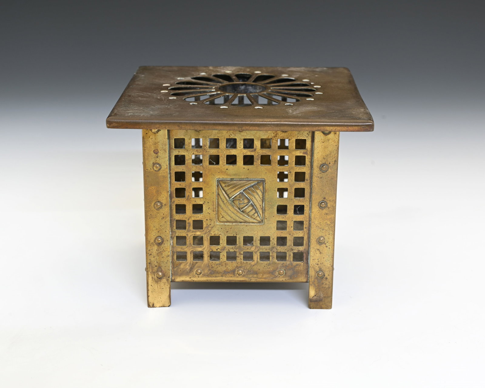 Margaret Gilmour, a Scottish Arts and Cr: Margaret Gilmour, a Scottish Arts and Crafts Glasgow School brass burner trivet, reticulated cuboid form with rivetted edges, central embossed rose motifs within pierced trellis sides, removable wide