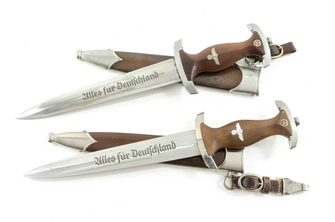 Two WWII German SA Daggers: Description Standard Serivce Dagger for Storm Troops, Germany World War Two. Each with leather hangers, wood hilts, painted steel scabbards, and double edged sharpened steel blades with "Alles fur Deu