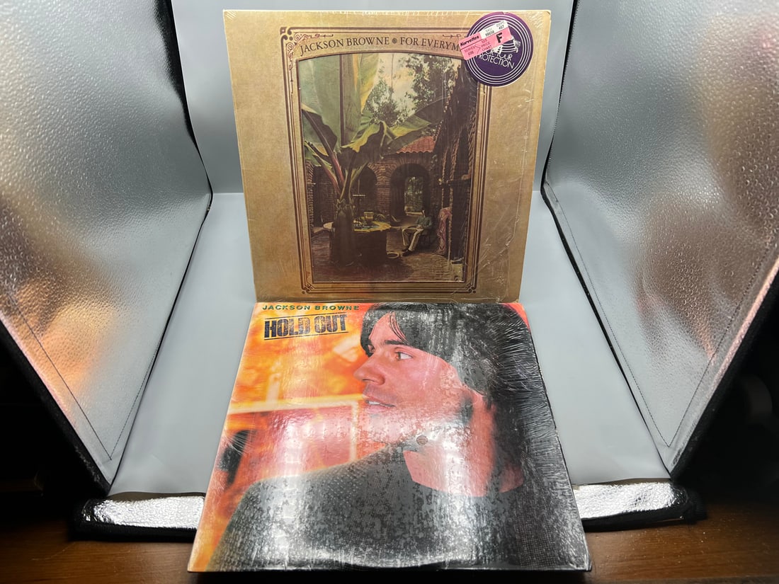 Jackson Browne (2 LP Lot): For Everyman (1976), repress, die-cut cover/picture sleeve, in original: Jackson Browne (2 LP Lot): For Everyman (1976), repress, die-cut cover/picture sleeve, in original shrinkwrap; and Hold Out (1980), in original shrinkwrap - Records have not been tested by the auction