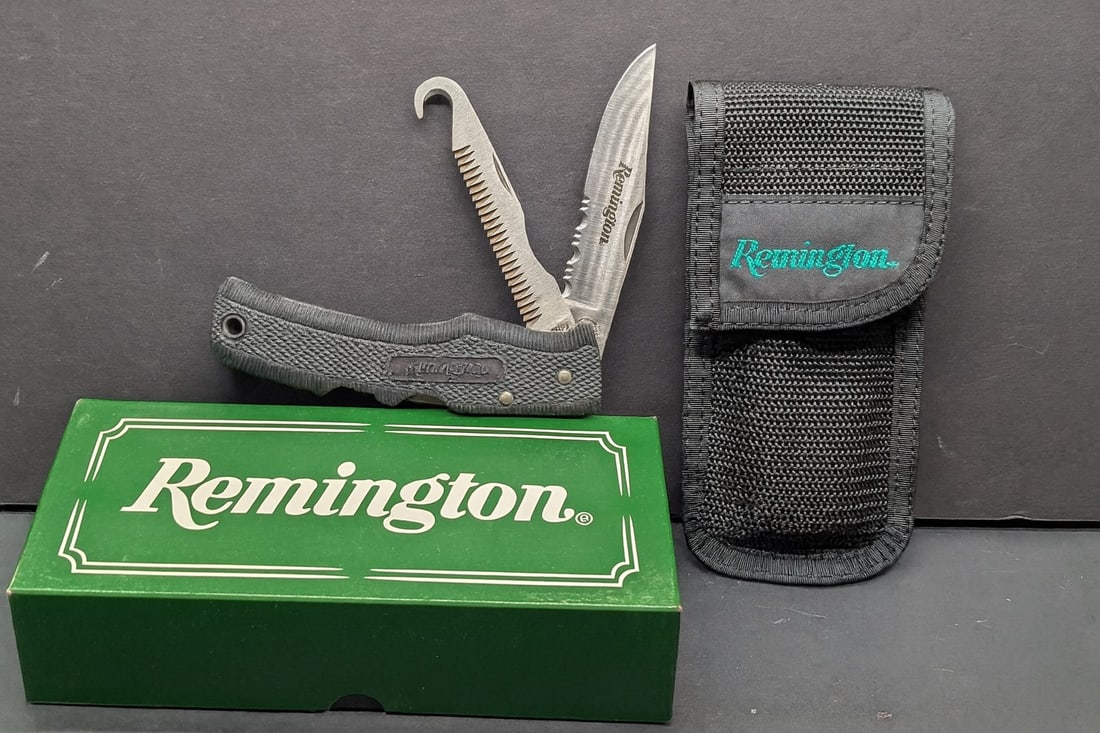 Remington Grizzly - 2 Blades w/ Gut Hook, Saw and Double Lookback and Sheath with Original Box: Two?blade lock?back hunter featuring a 3?? clip?point blade (partial serrations, Remington logo) and a separate combo bone saw?/?gut?hook blade. Black textured polymer handle with molded Remington ova