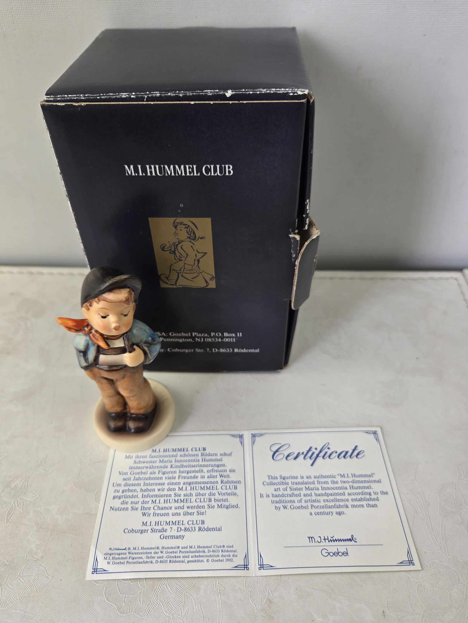 1989 Goebel M.I. Hummel Lucky Fellow Hum 560 (M.I. Hummel Club 1992/93): A 1989 Goebel M.I. Hummel ceramic figurine, 'Lucky Fellow' (Hum 560), issued for the M.I. Hummel Club Membership Year 1992/93. This charming piece depicts a boy in a black cap, blue jacket, and brown