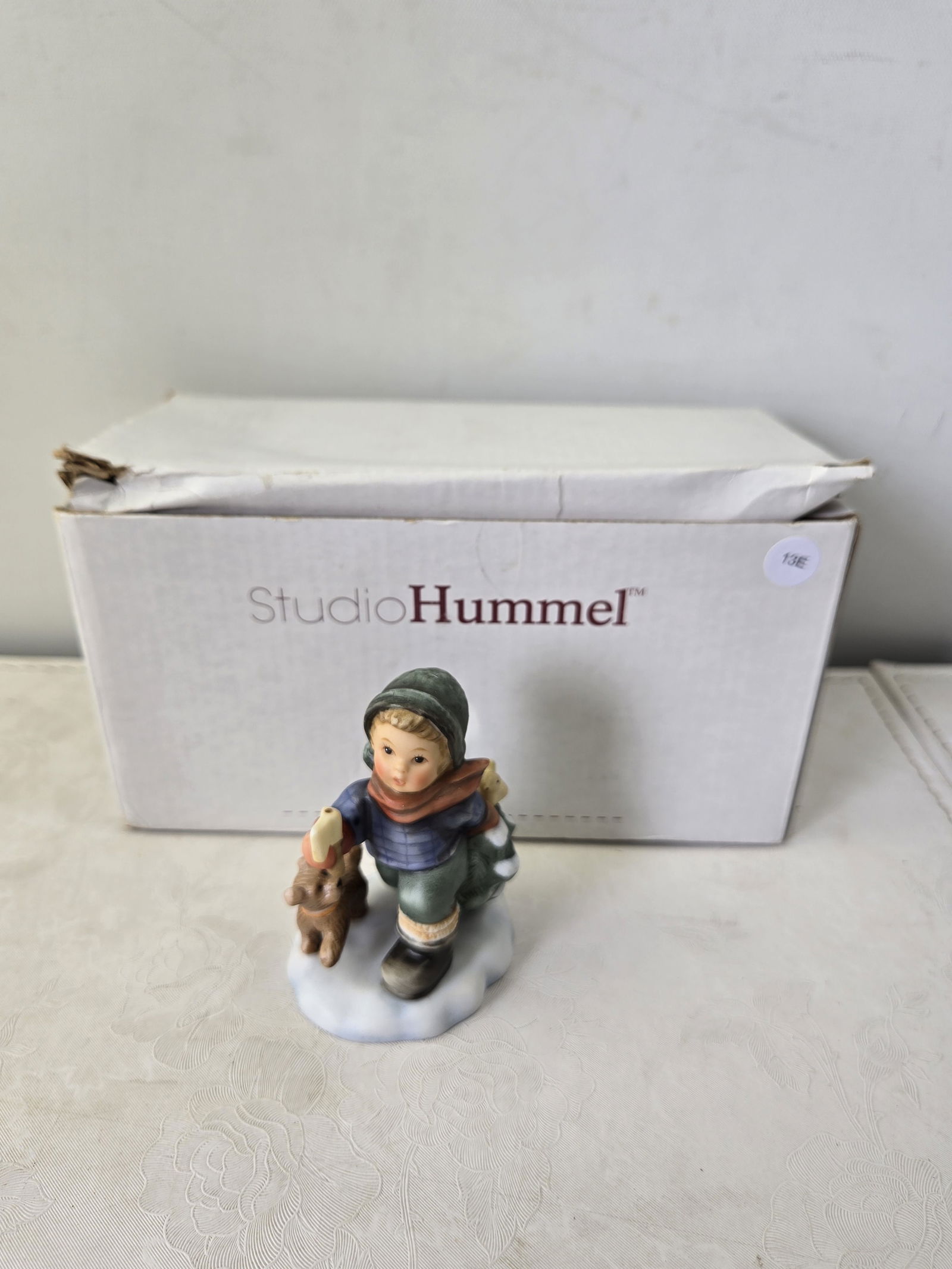 2001 Goebel Studio Hummel "O Tannenbaum" BH 47/P Porcelain Figurine: This lot features a 2001 Goebel Studio Hummel "O Tannenbaum" BH 47/P porcelain figurine. The figurine depicts a charming child dressed in winter attire, holding an axe, and pulling a small evergreen t
