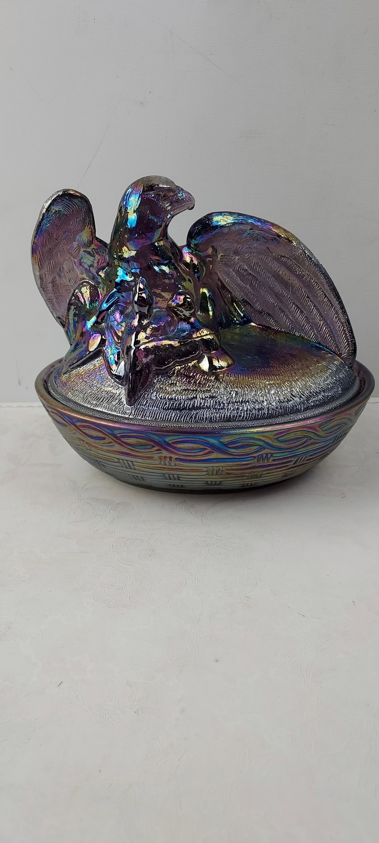Circa 1991 Fenton Art Glass Amethyst Carnival Glass Eagle on Nest Covered Dish: A captivating two-piece covered dish by Fenton Art Glass, crafted from deep amethyst (purple) carnival glass. The lid features a prominent figural eagle, meticulously detailed with textured wings and 