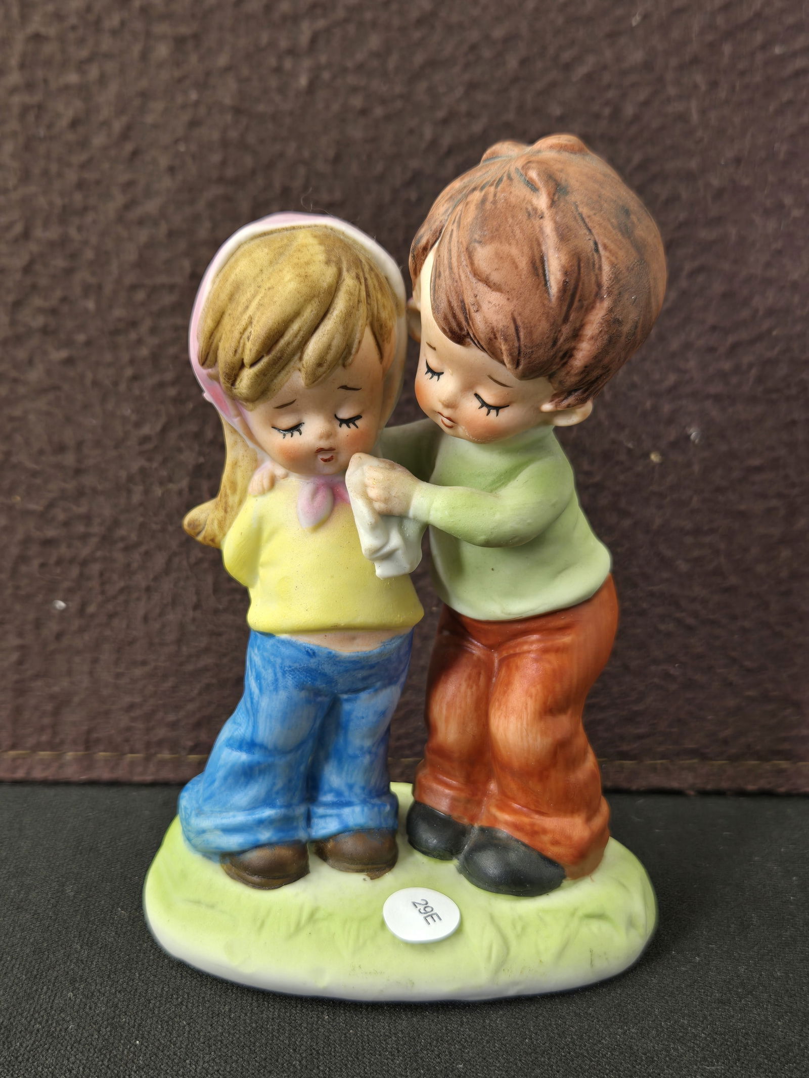 Vintage Decorana INC. Dallas Texas Japan Hand-Painted Bisque Porcelain Boy & Girl Figurine: A charming vintage hand-painted bisque porcelain figurine by Decorana INC., Dallas, Texas, Japan. This endearing piece depicts a young boy with brown hair, dressed in a green shirt and orange pants, t