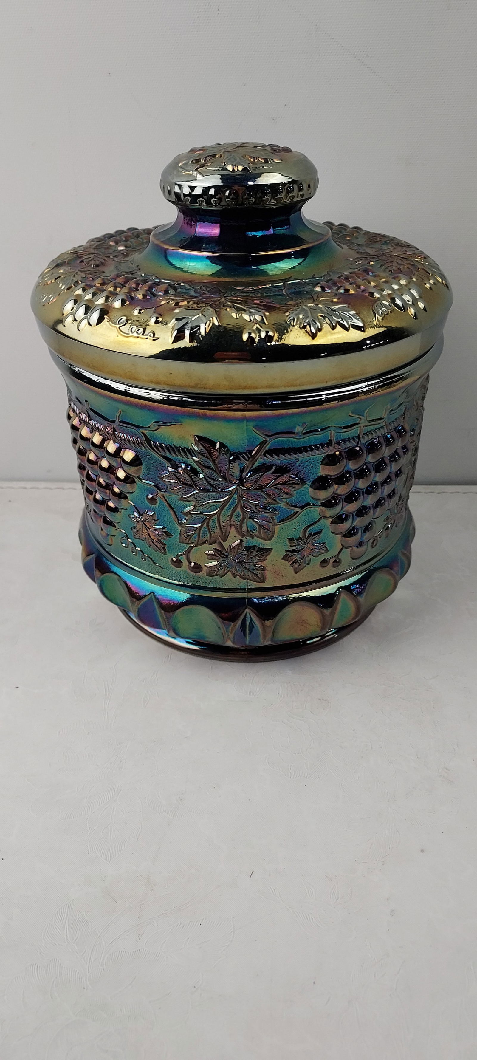 1989 Fenton Presznick's Carnival Glass Museum Grape & Cable Amethyst Carnival Glass Humidor/Tobacco: This 1989 Fenton Presznick's Carnival Glass Museum Grape & Cable Amethyst Carnival Glass Humidor/Tobacco Jar is a two-piece lidded container, crafted by Fenton. It features a vibrant iridescent finish