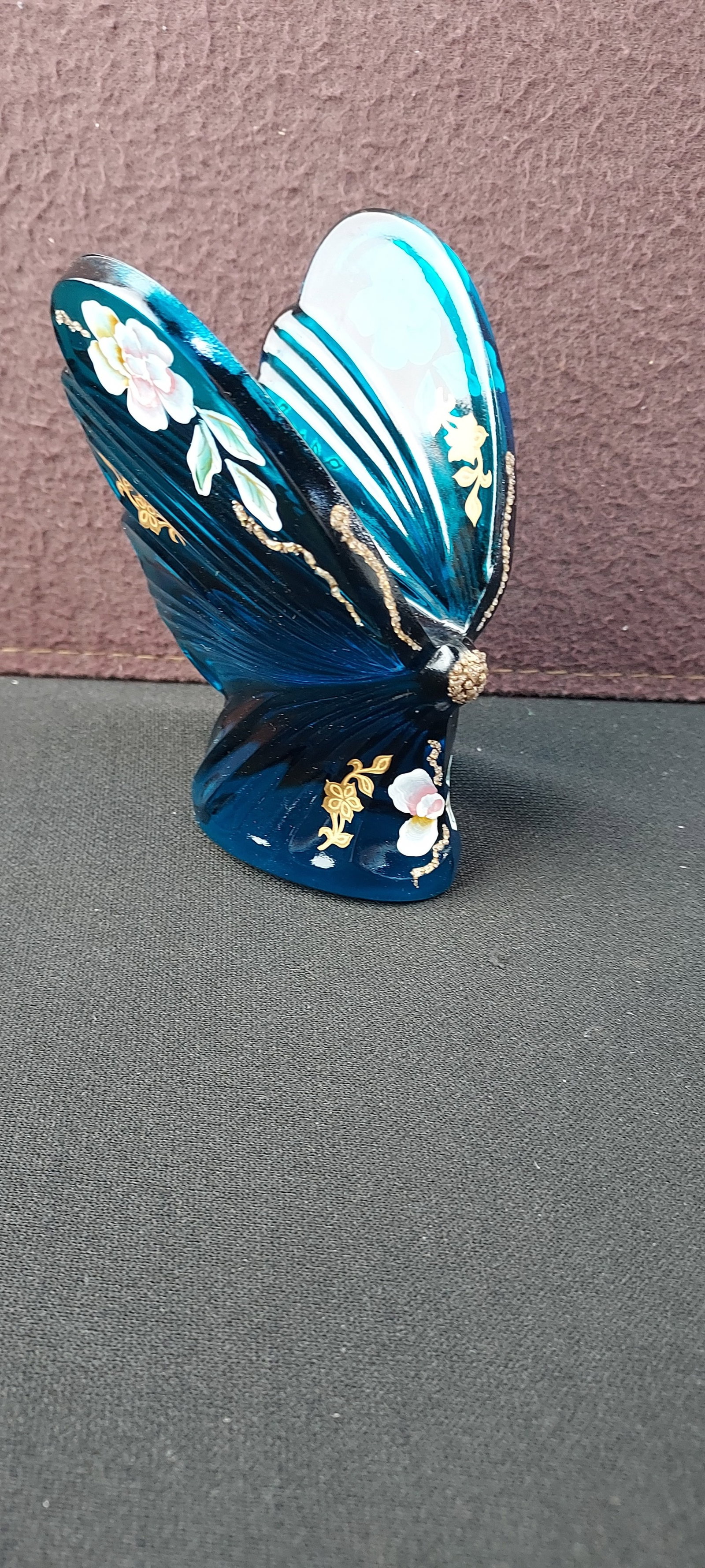 Fenton Art Glass Blue Floral Butterfly Hand Painted Figurine: This offering presents a Fenton Art Glass Blue Floral Butterfly Figurine. Crafted from translucent blue glass, the piece features finely molded details simulating natural wing veins. The figurine is m