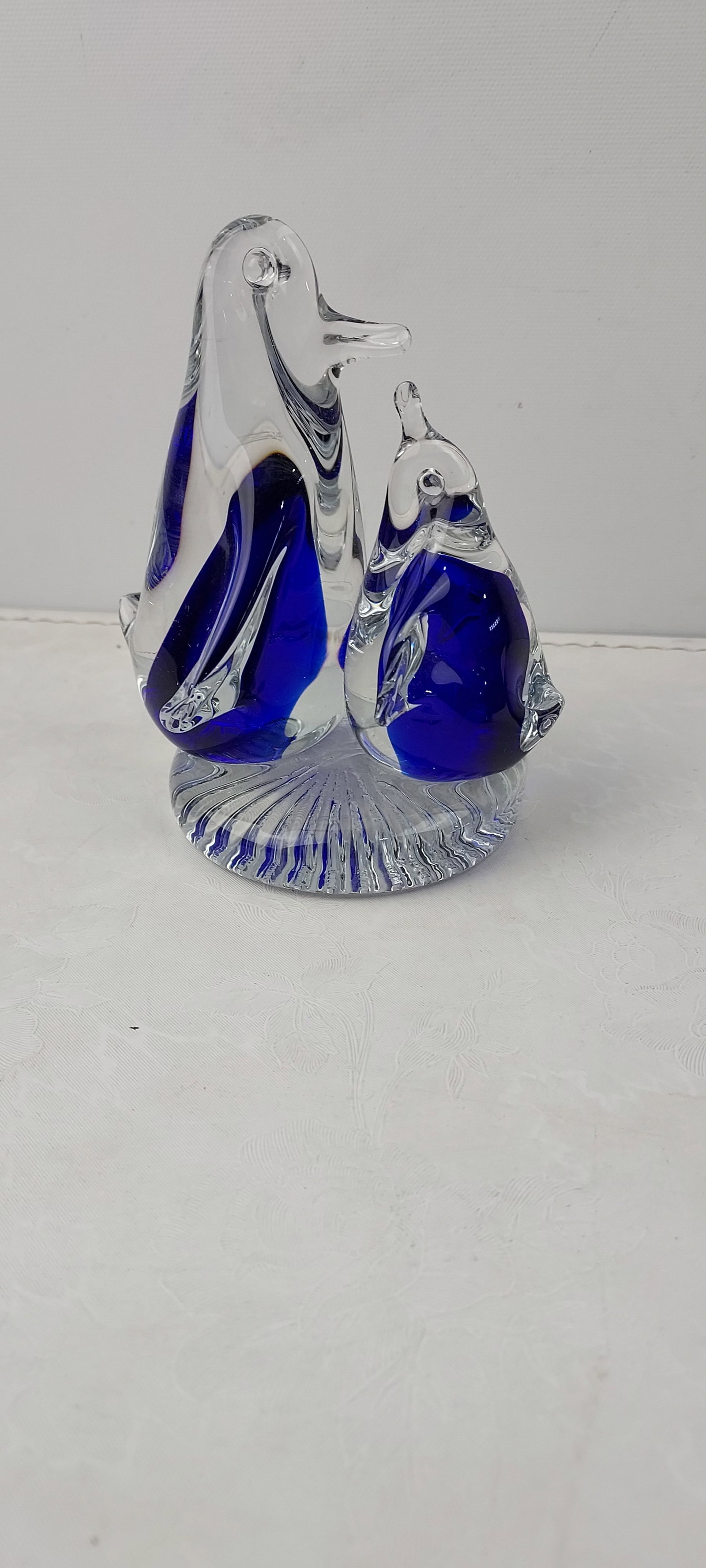 Art Glass Clear and Cobalt Blue Mother & Baby Penguins Sculpture Paperweight: A decorative art glass sculpture featuring two penguin figures, one larger and one smaller, positioned on a unified circular base. Crafted from clear glass, both penguins incorporate distinct internal