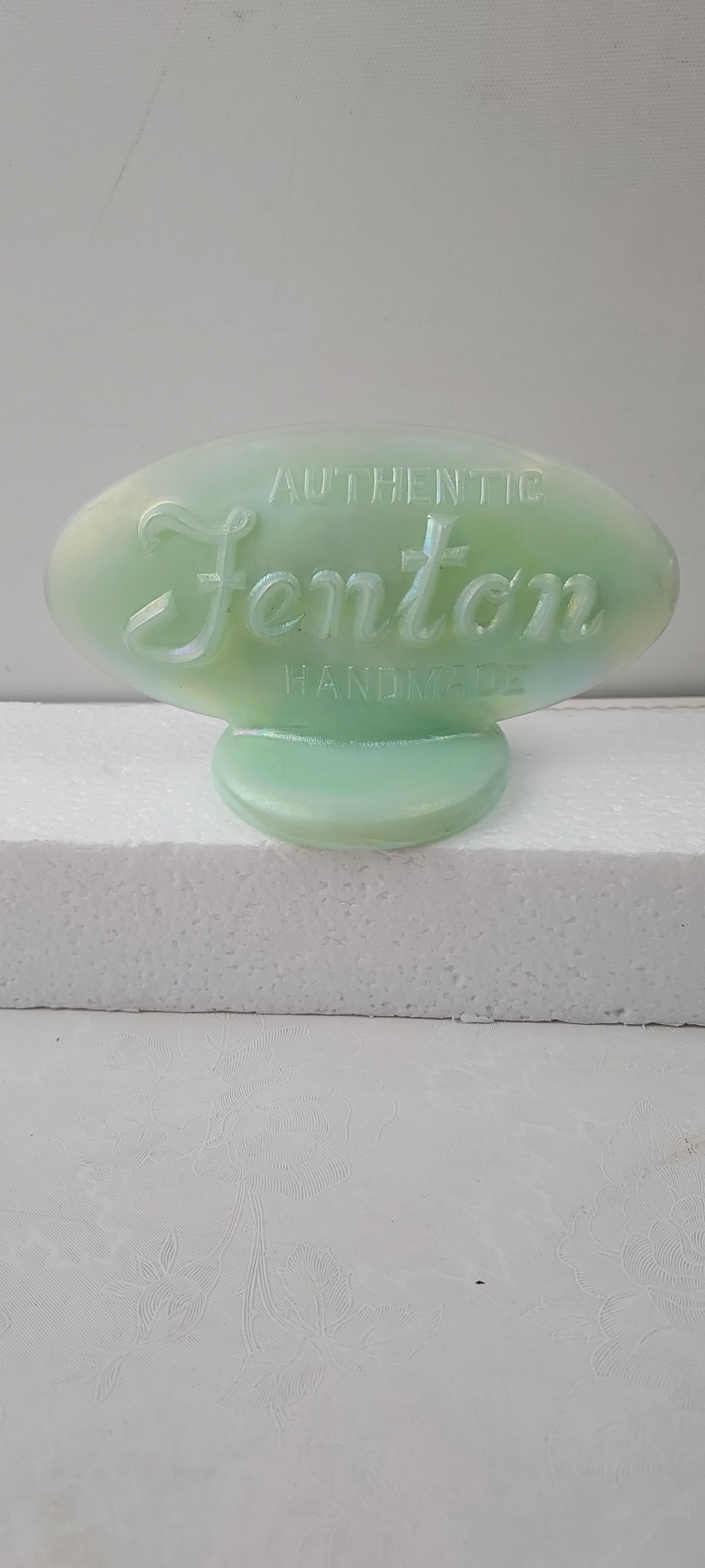 Fenton Sea Mist Green Iridescent Glass Oval Dealer Logo Sign Paperweight 9499 GE: This is an authentic Fenton Sea Mist Green Iridescent Glass Oval Dealer Logo Sign, identified by model number 9499 GE. This decorative glass piece features an oval-shaped top section resting on a circ