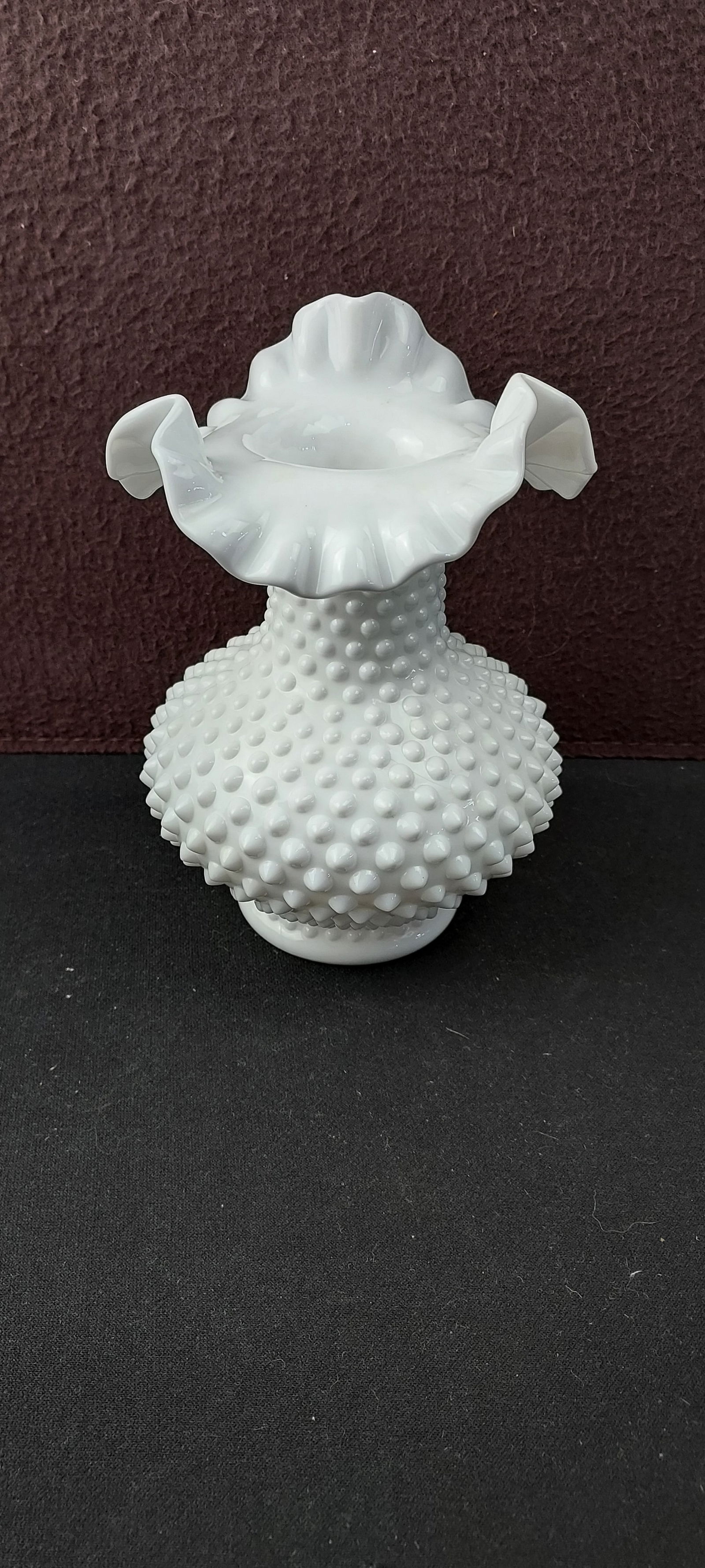 Vintage Fenton White Milk Glass Hobnail Ruffled Crimped Vase: A vintage Fenton white opaque milk glass vase, featuring a distinctive hobnail pattern of raised, rounded bumps covering its bulbous body and cylindrical neck. The top opening presents a widely flared