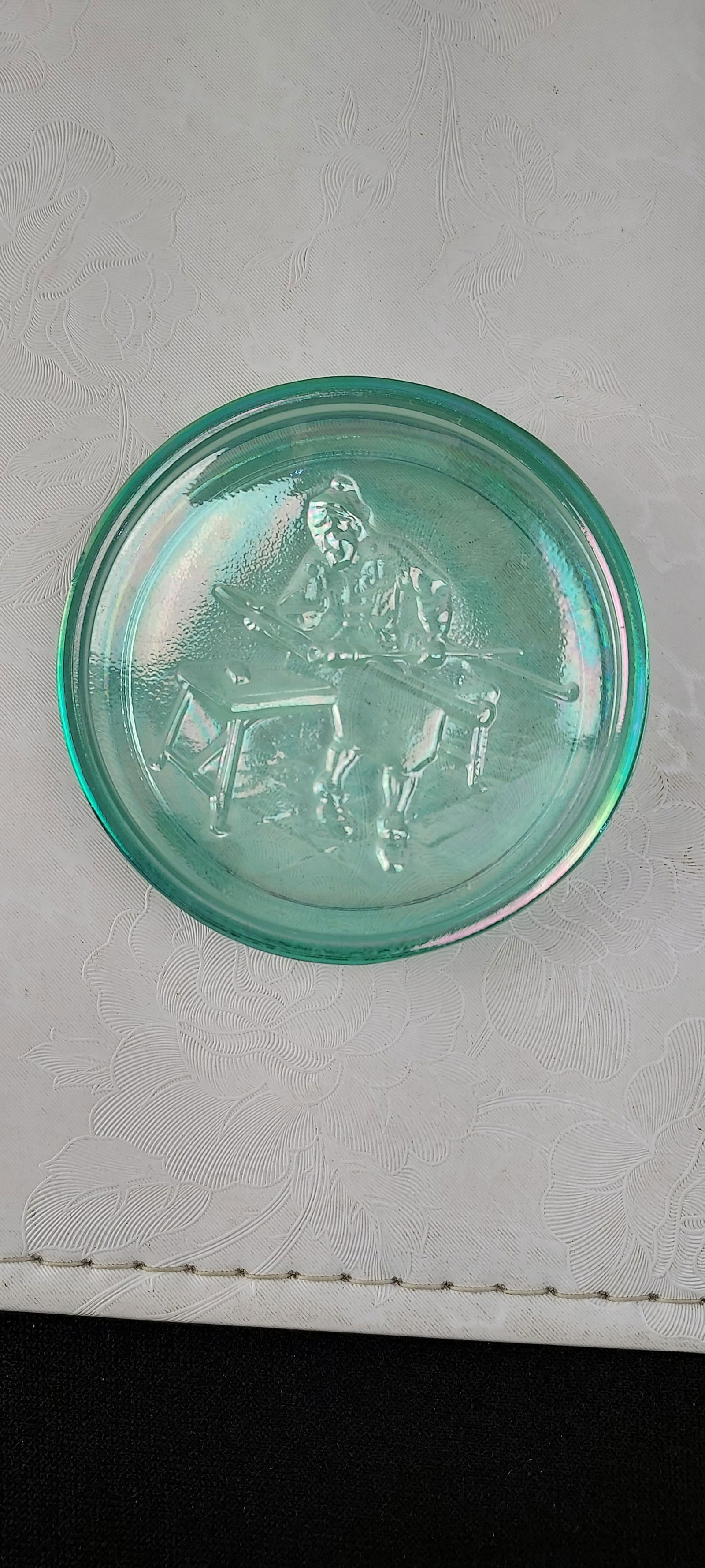 Vintage Spirit of '76 Green Carnival Glass Coaster: A vintage carnival glass coaster or small plate, featuring a distinctive embossed central design depicting a figure consistent with the fifer from the iconic "Spirit of '76" painting. The glass exhibi