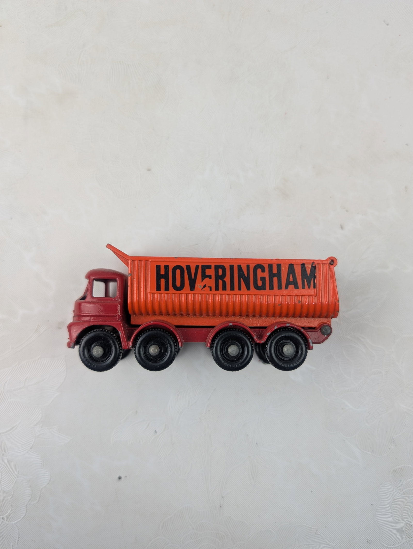 Vintage Matchbox Lesney No. 17d Foden Hoveringham Tipper Truck: A vintage Matchbox Lesney No. 17d Foden Hoveringham Tipper Truck, a die-cast toy manufactured in England by Lesney. This model features a red cab and chassis with an orange tipper bed, emblazoned with