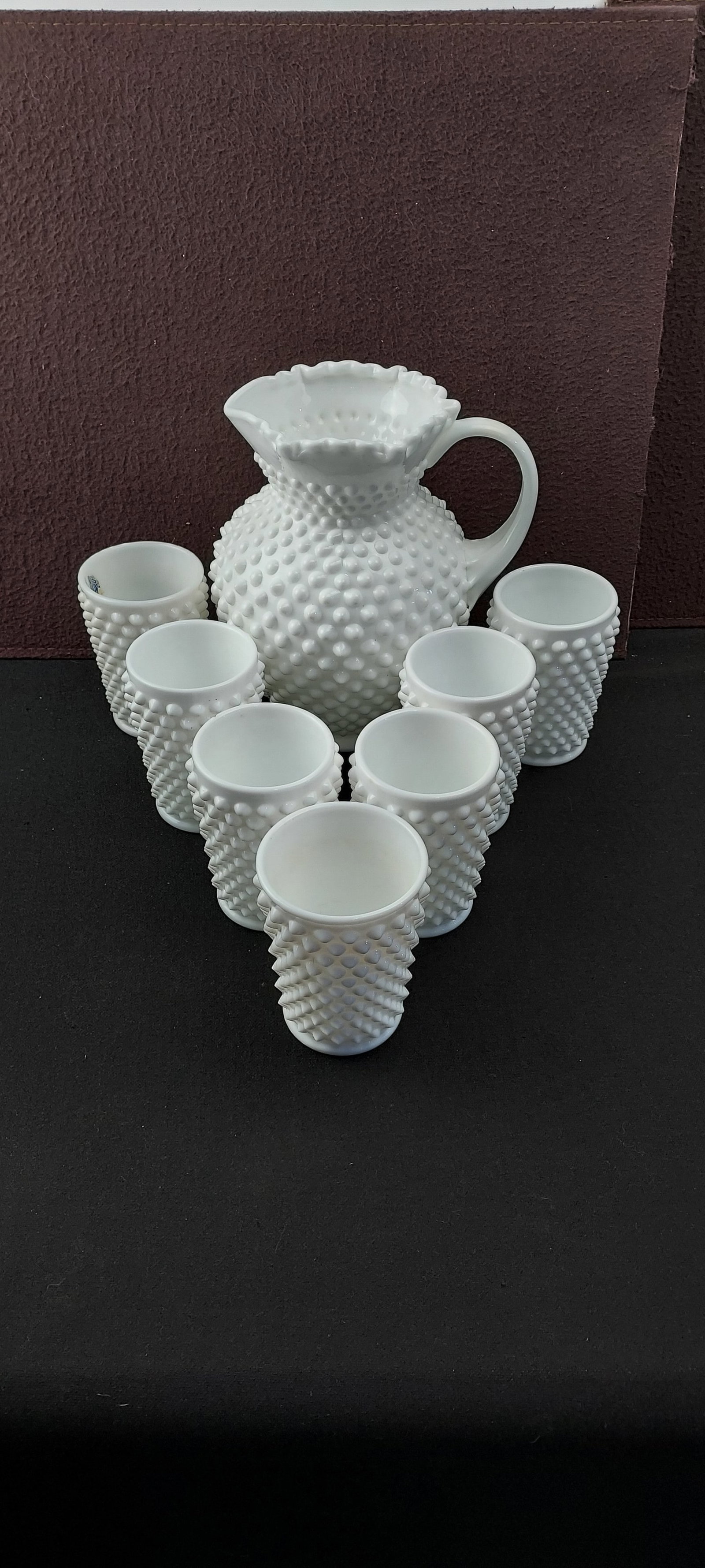 1950s Fenton Hobnail Milk Glass Ball Pitcher and Eight Tumblers Set: A vintage mid-20th century Fenton Art Glass Company 'Hobnail' milk glass serveware set. This complete set comprises one 'Ball Pitcher' featuring a distinctive ruffled rim and eight matching tumblers.