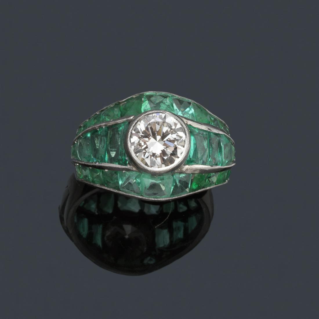Ring with central brilliant in platinum setting with: Ring with central brilliant of approx. 2.50 ct in platinum setting with front design of emeralds in channel. Brilliant estimated to be of color I/J and clarity SI.
