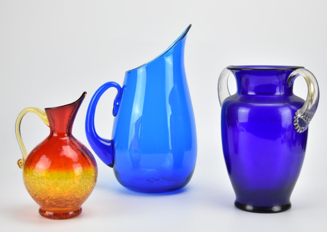 3 Piece Colored Glass Vessels: 3 Colored Glass Vessels: - A cerulean/ light blue Blenko pitcher with long pointed spout - A bulb-shaped orange & red crackle glass pitcher with pointed spout and thin handle - A dark blue twin handle