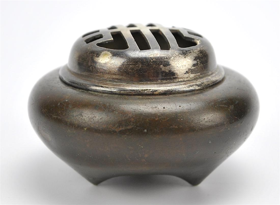 A Japanese Bronze Tripod Censer and Cover,19th C.: A small Japanese bronze tripod censer with mirrored smoke openings in the lid. D.3 3/8in.(8.5cm), H.1 5/8in.(4cm) Condition: in good condition with expected minor wear