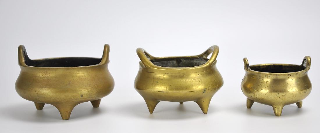 Three Chinese Bronze Tripod Censers: A set of 3 bronze tripod censers of similar cauldron form with handles on either side of the mouth and matching 6 character marks underneath. D: 3 5/8" (9.3cm) Smallest | 5" (12.2cm) Largest Condition