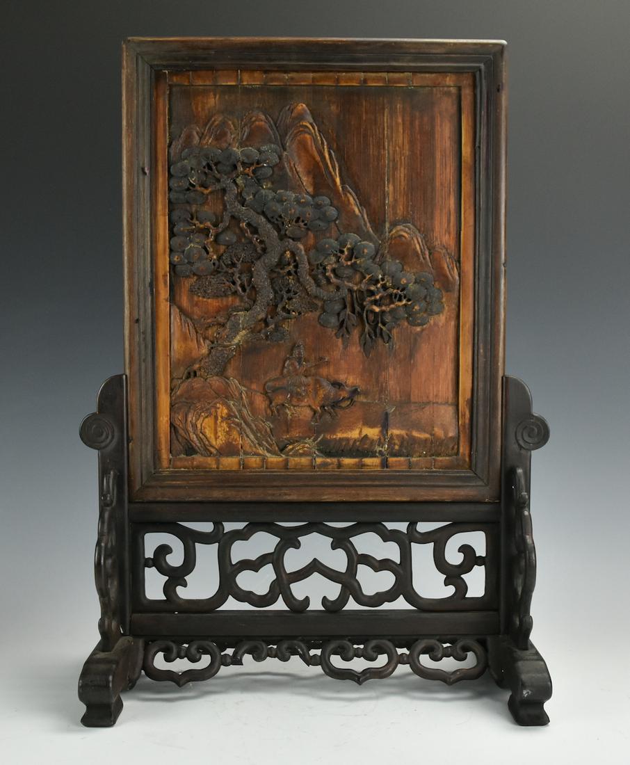 Wooden Screen on Sculpted Stand: Figure w/ Ox: A carved wooden screen depicting a figure on the back of an ox taking a path down the mountains with a gnarled pine above them, vertically oriented with decorative sculpted stand adorned with ruyi sha
