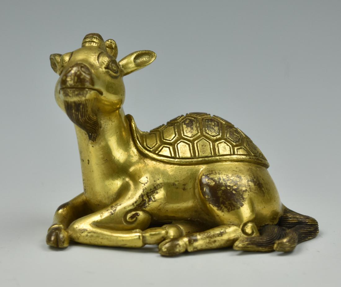 Chinese Mythical Gilt Bronze Deer, Qing D.: A gilt, bronze, deer-like mythical beast, rests on the ground with four legs curled together. There is a horn on the head a beard on the chin, and a turtle shell on the back. L: 3.2in.(8cm); H: 2.55in