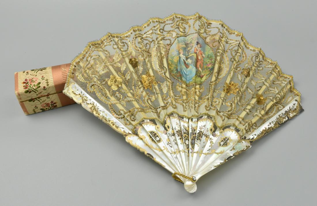 An Antique English Mother of Pearl Fan: An antique British/ European lace & mother of peal folding fan with a central painted paper scene of a boy playing a flute to a girl beside a fountain, with beaded & painted gold embellishments, with 