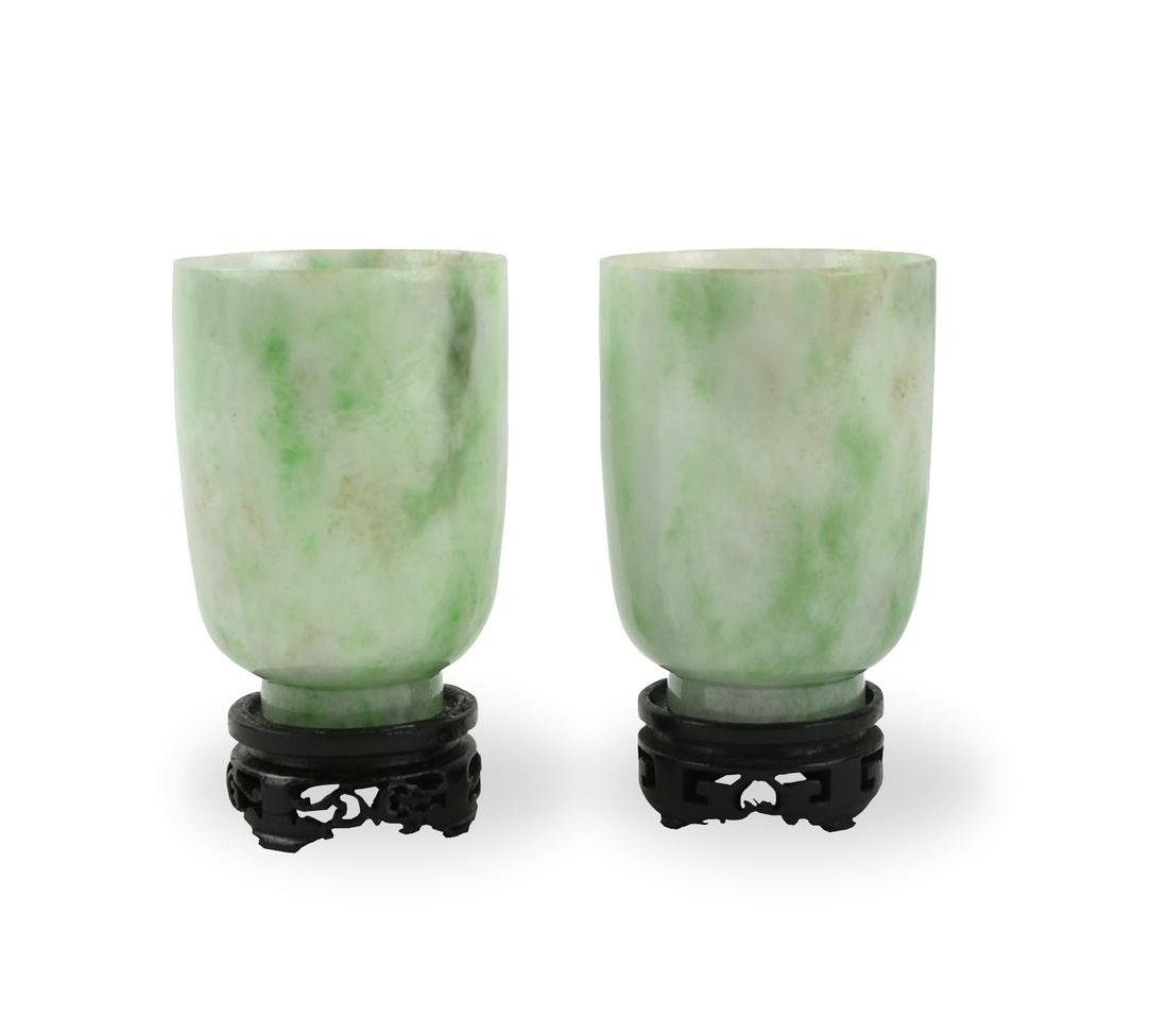 Pair of Chinese Jadeite Cups, Qing Dynasty: Chinese ,Qing Dynasty, each with deep rounded sides rising from a concave base, the translucent pale green stone suffused with emerald and darker green inclusions, wood stands H: 2.6"(6.5cm) D: 1.8"(4
